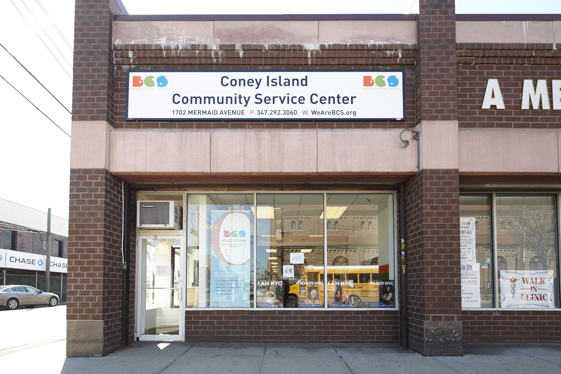 The brick front facade of the BCS Coney Island Office. An air conditioner sits above the glass front door, next to three windows.