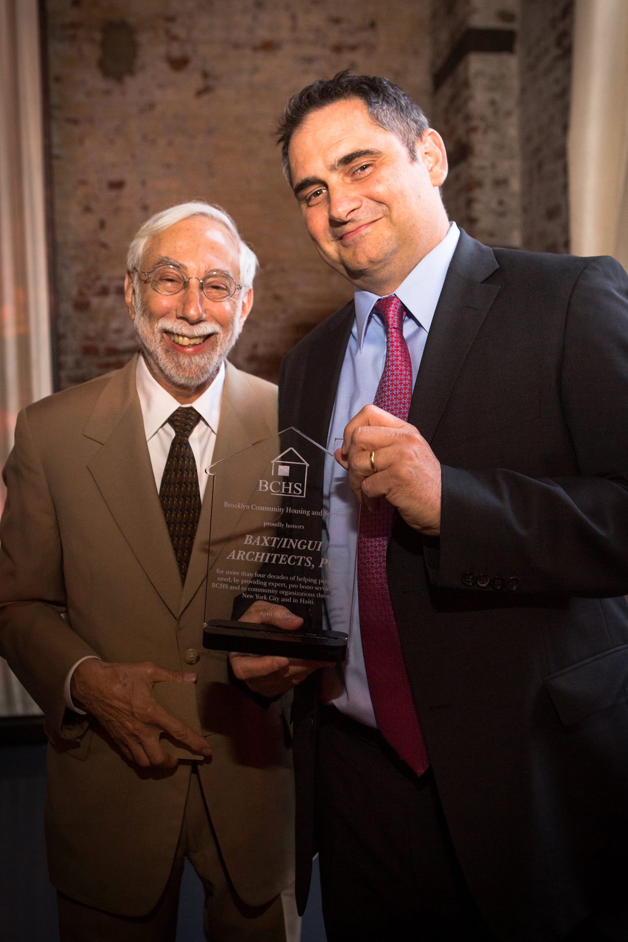 Ben Baxt on the left and Mike Ingui on the right smile at the camera, holding the BCHS award Baxt Ingui won.