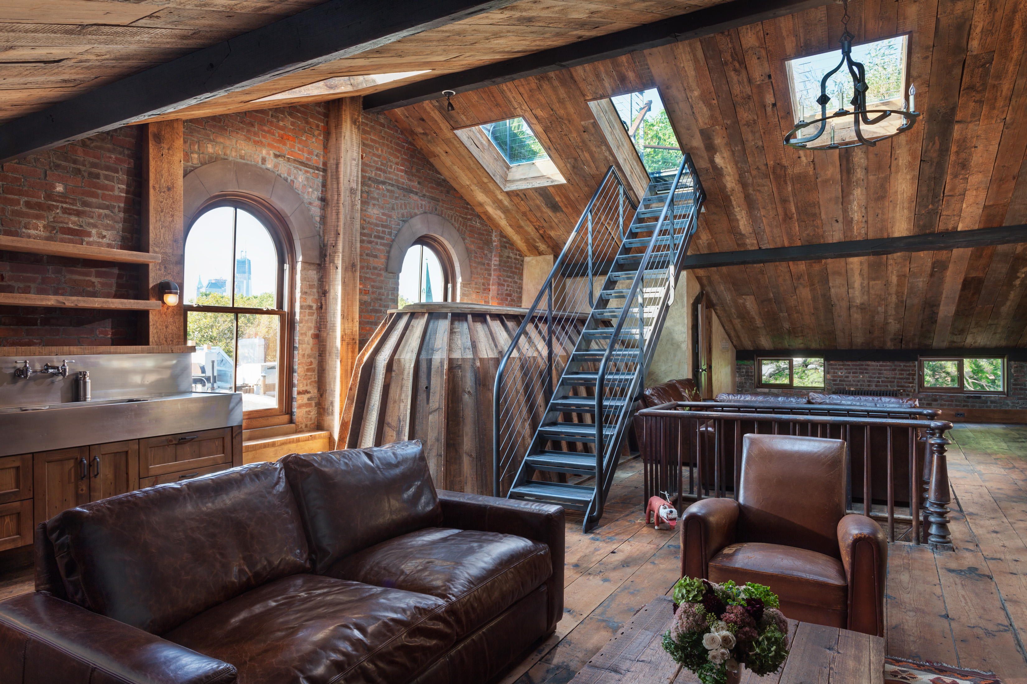 Attic of a Brooklyn Heights home with four windows, three skylights, a metal staircase leading to the roof, wood paneled ceiling and exposed brick walls.