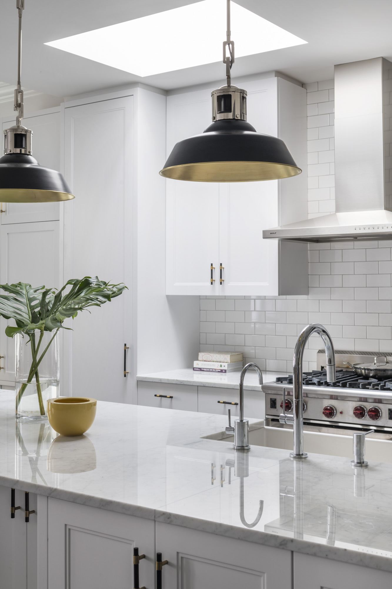Open, all-white kitchen with black pendant lights hanging above the kitchen island