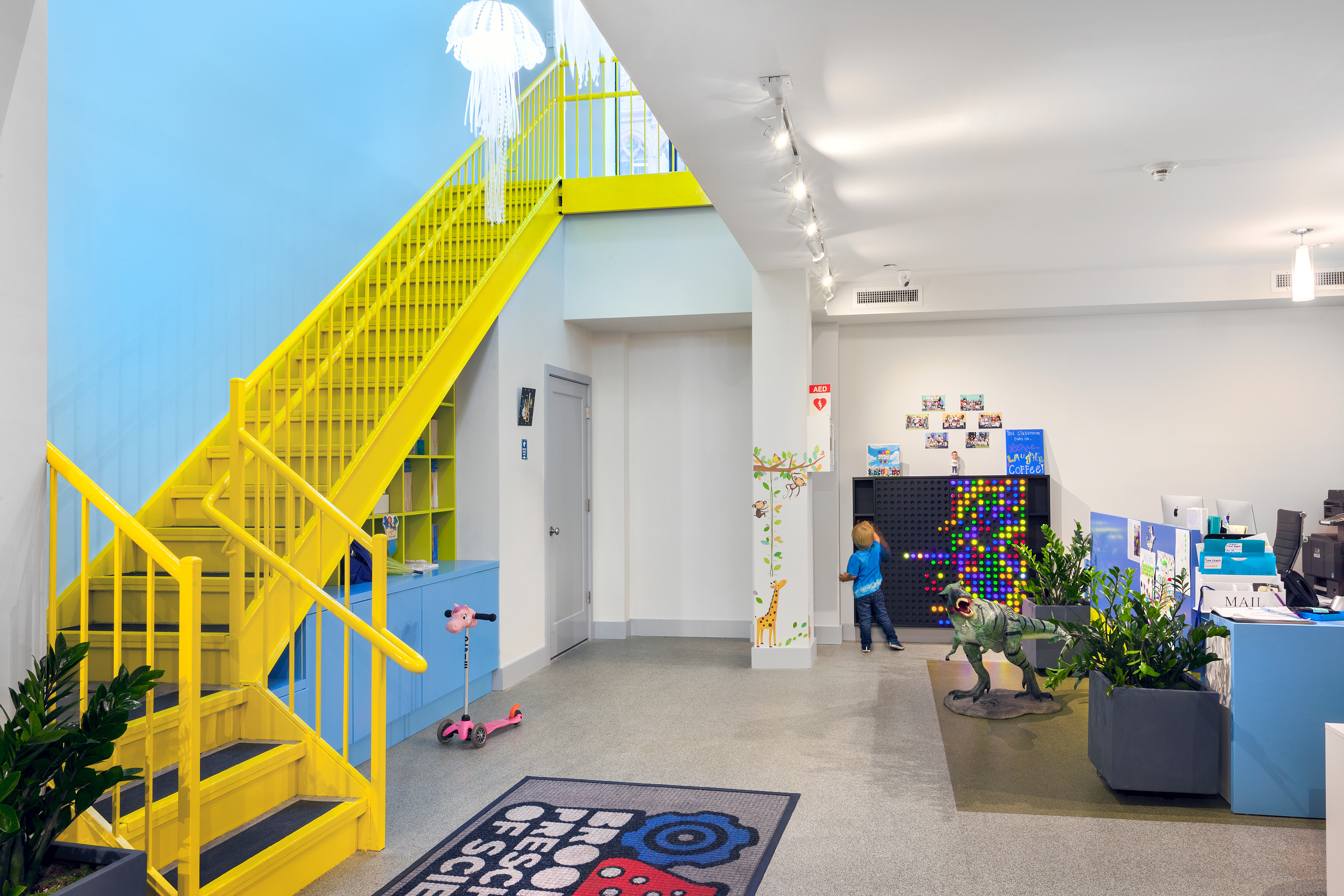 Bright yellow staircase leading to an office space with one bright blue accent wall and a jellyfish light.