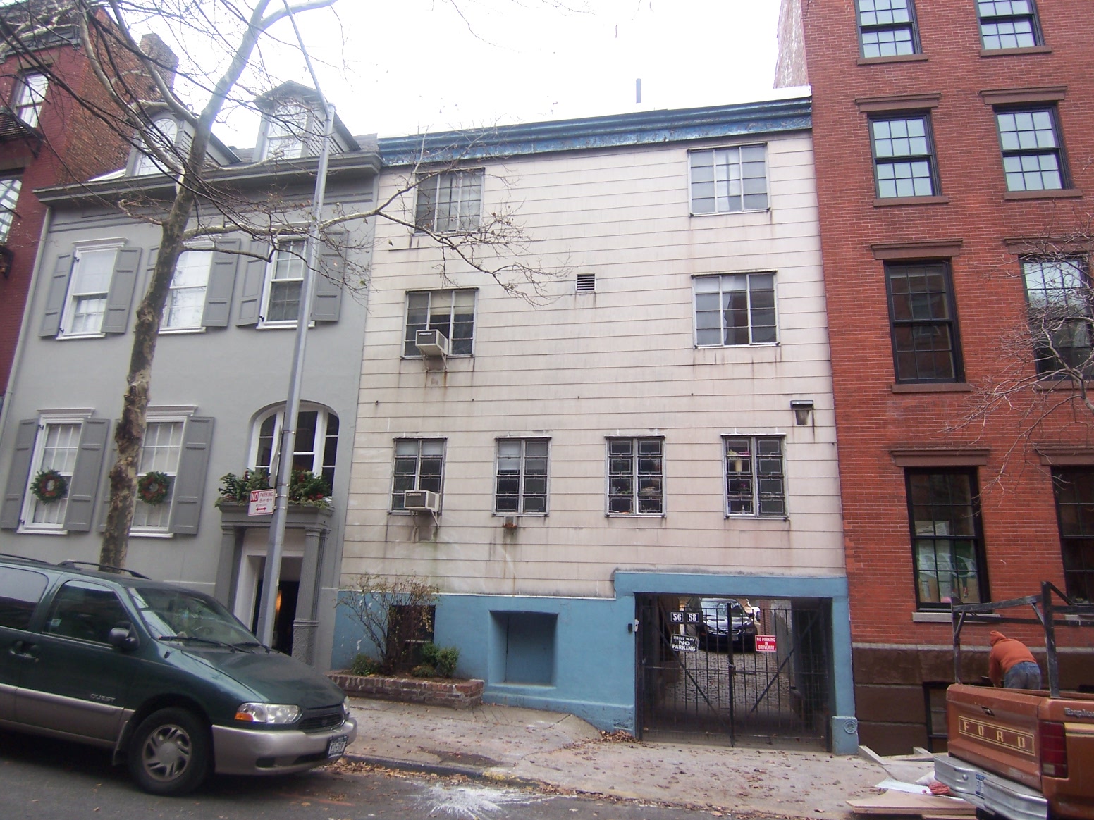 Front facade of a rowhouse with a garage, white siding, and blue-painted garden floor and transom