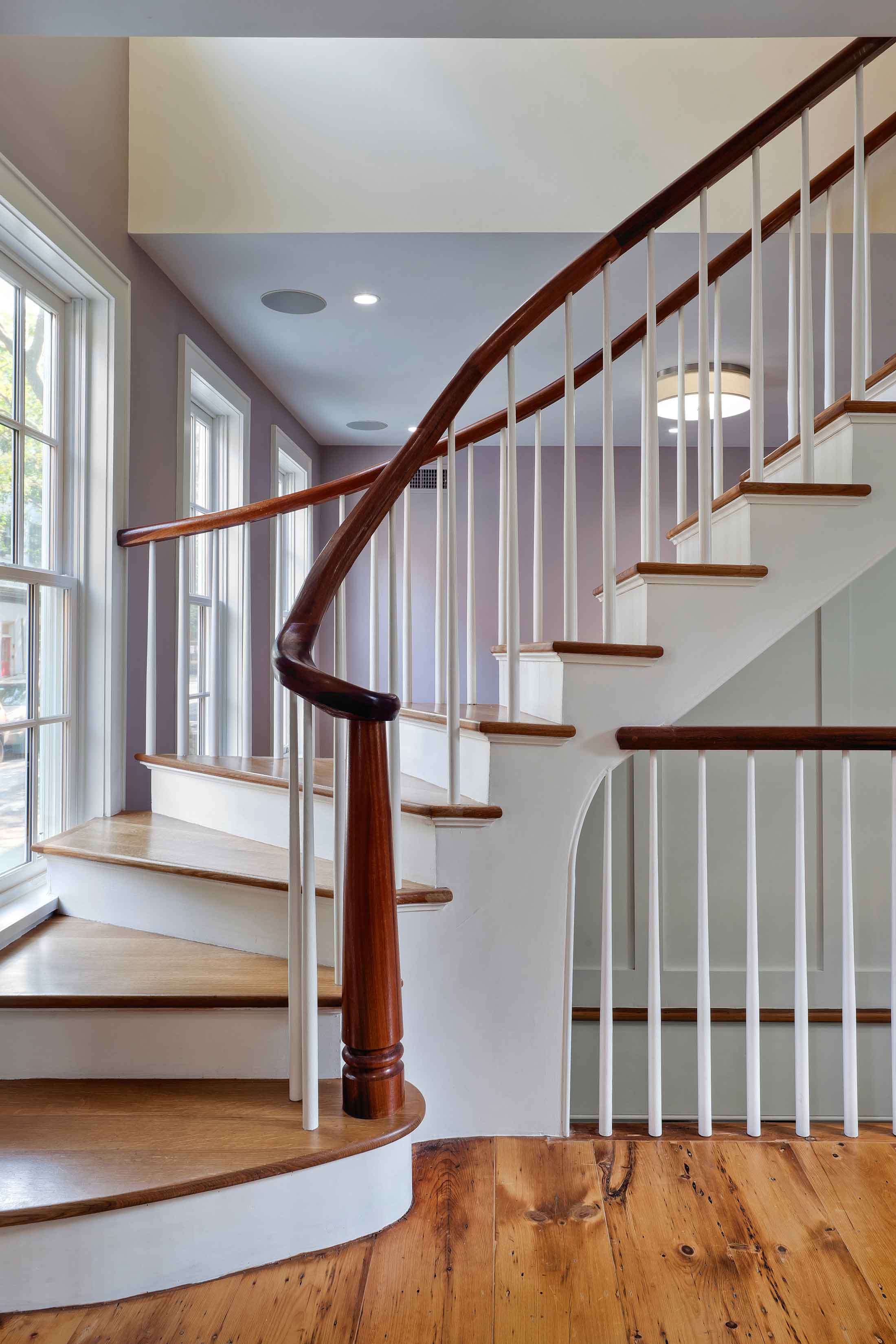 Detail image of a white painted wood staircase with natural finished handrails, treads, and newel post