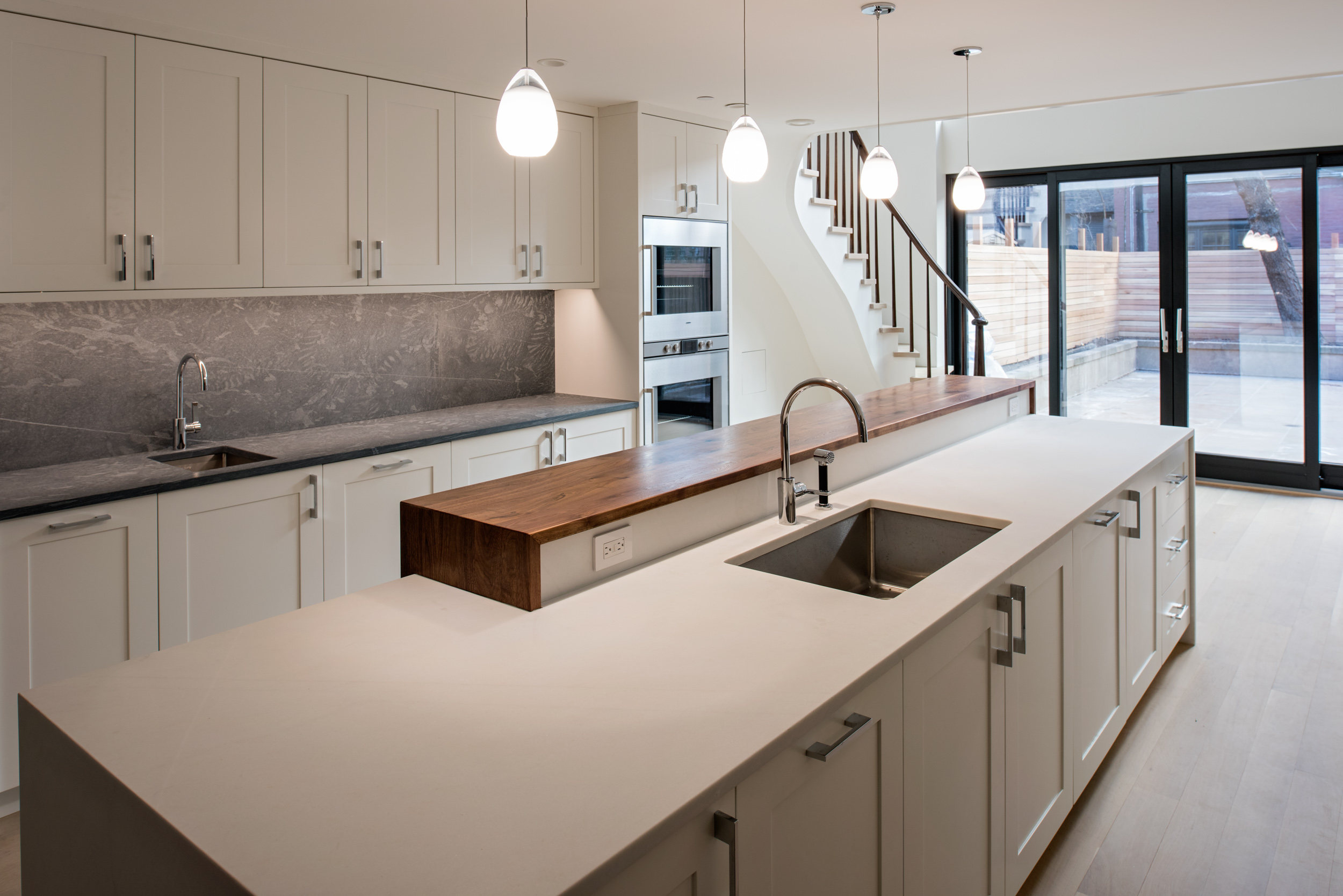 All white kitchen with four pendant lights and natural wood countertops in an Upper West Side Passive House