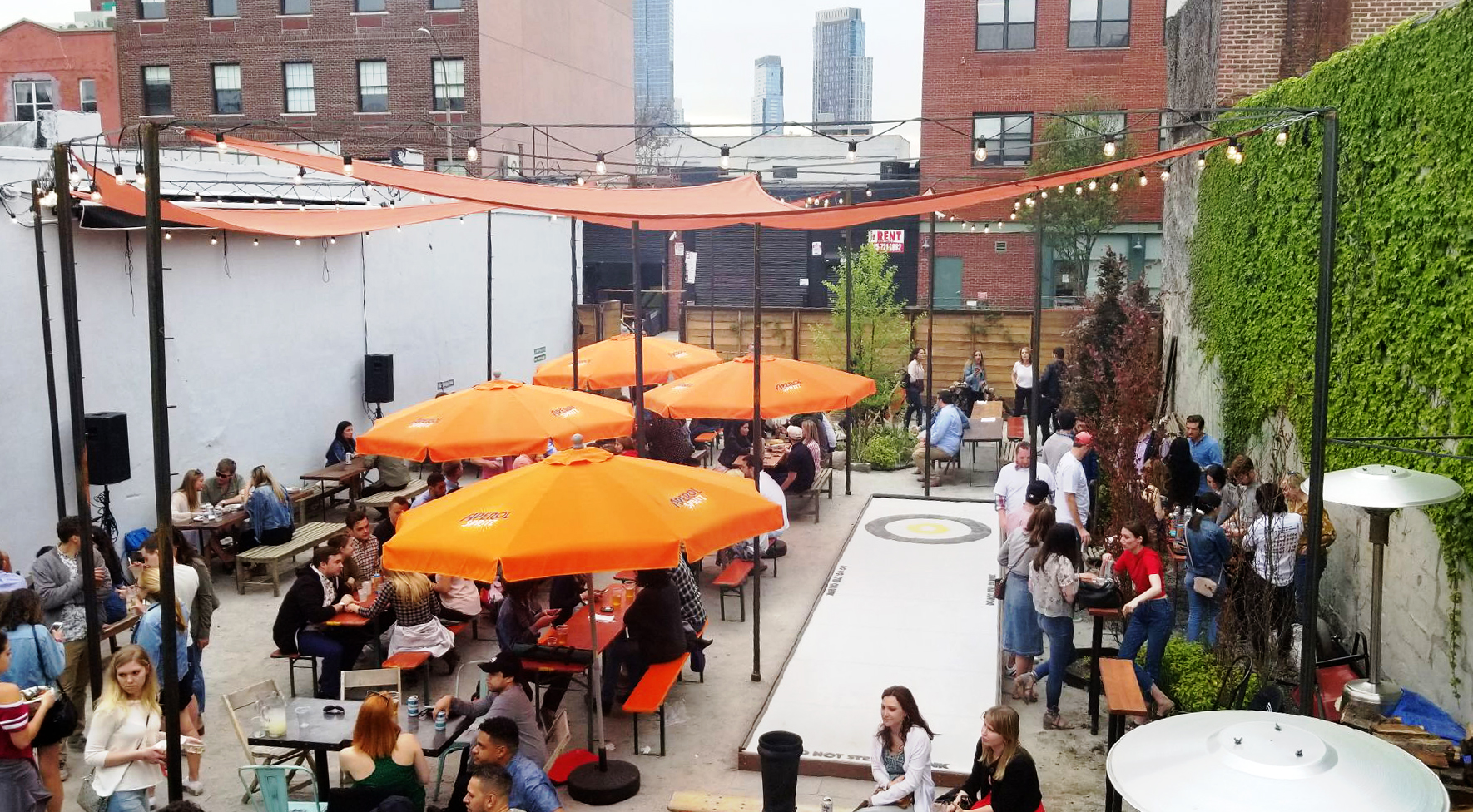 Courtyard of Parklife, with orange umbrellas and awnings and crowds of people talking and drinking.