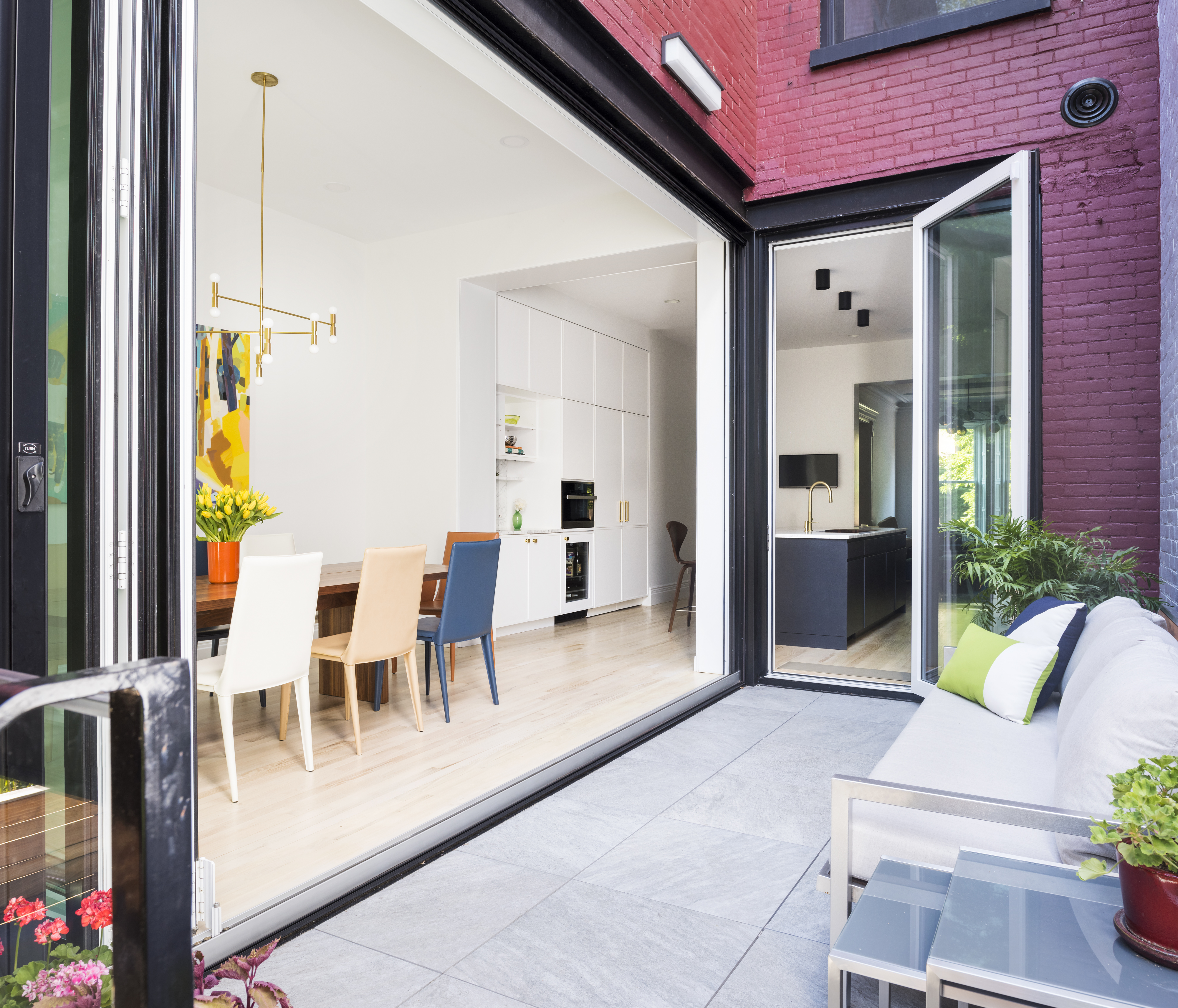 Rear façade of a red-painted brick townhouse with a large NanaWall open to the dining room and kitchen